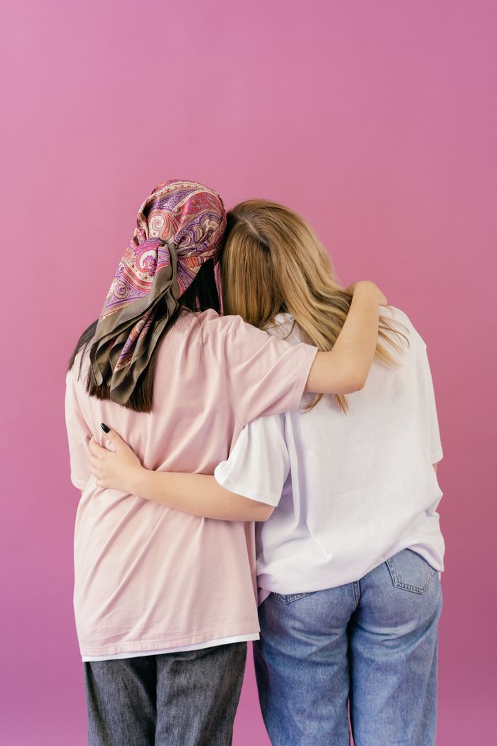 Two women share a comforting hug against a vibrant pink backdrop, symbolizing friendship and support.